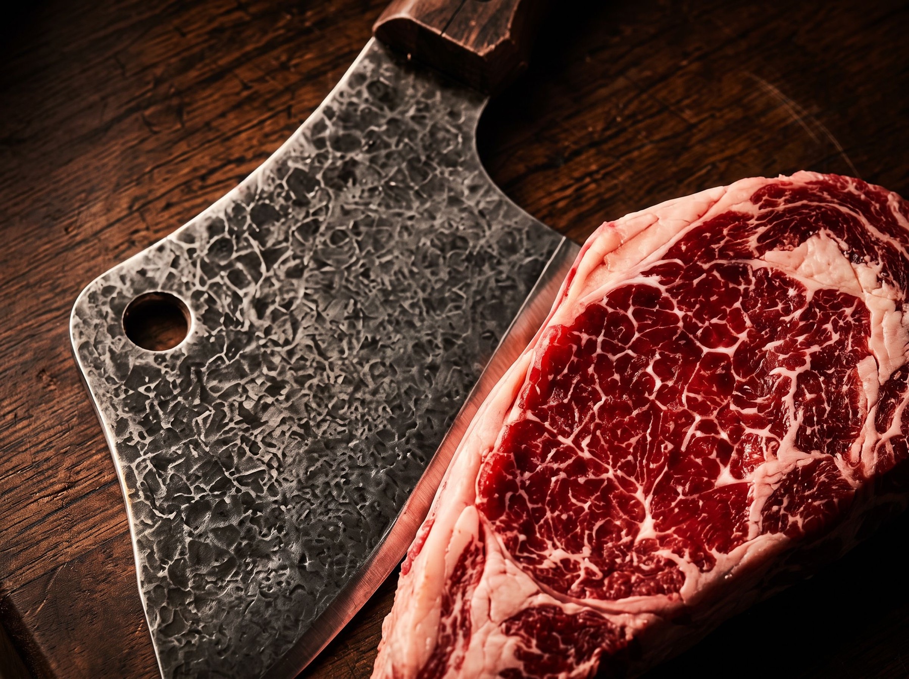 Hammered cleaver beside a marbled steak on the block